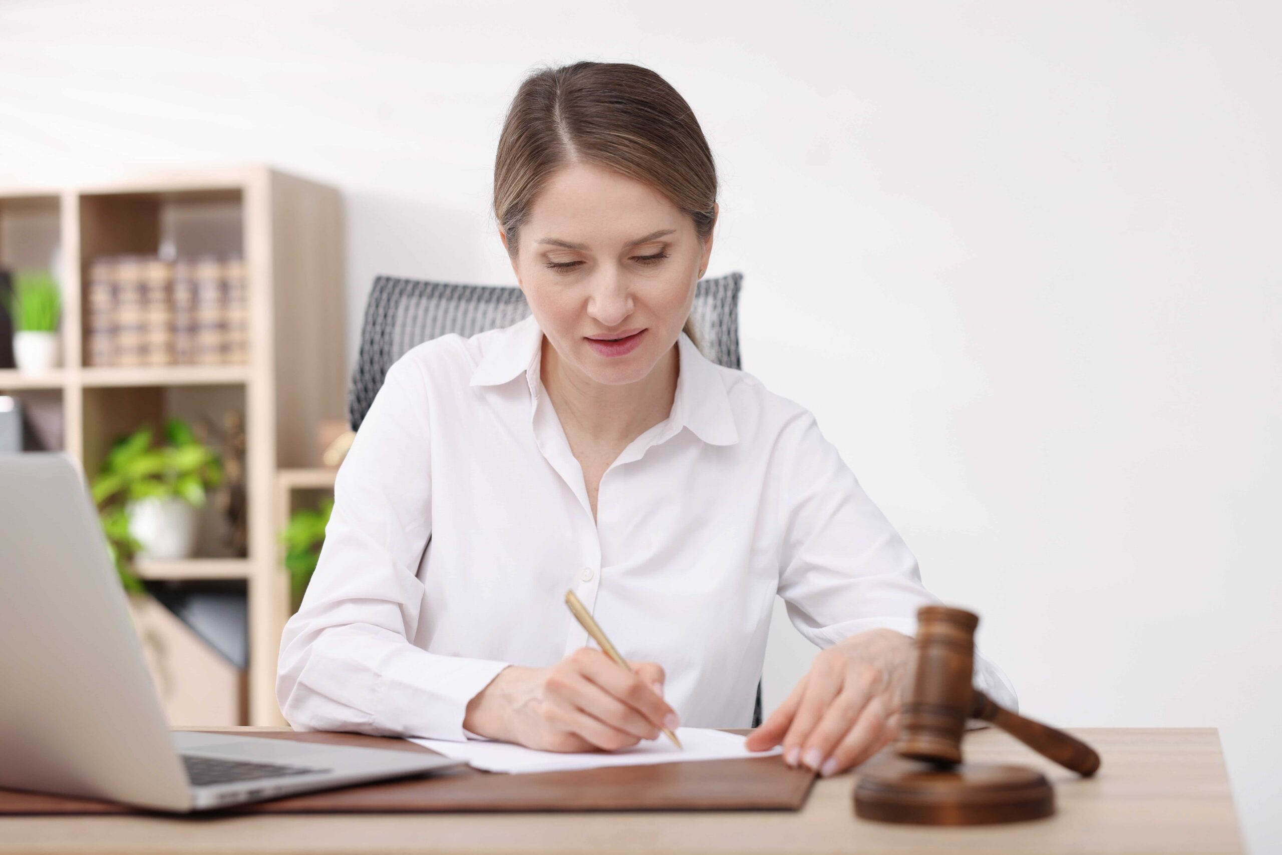 Professional woman writing at office desk beside a wooden gavel